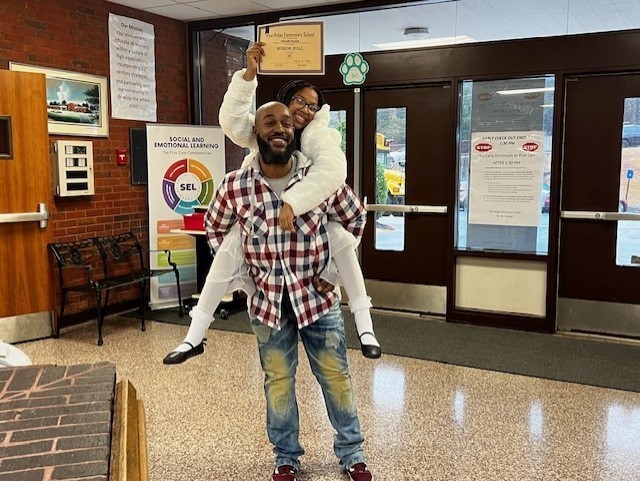 Father holding his daughter on his back with her awards on Honors Day.
